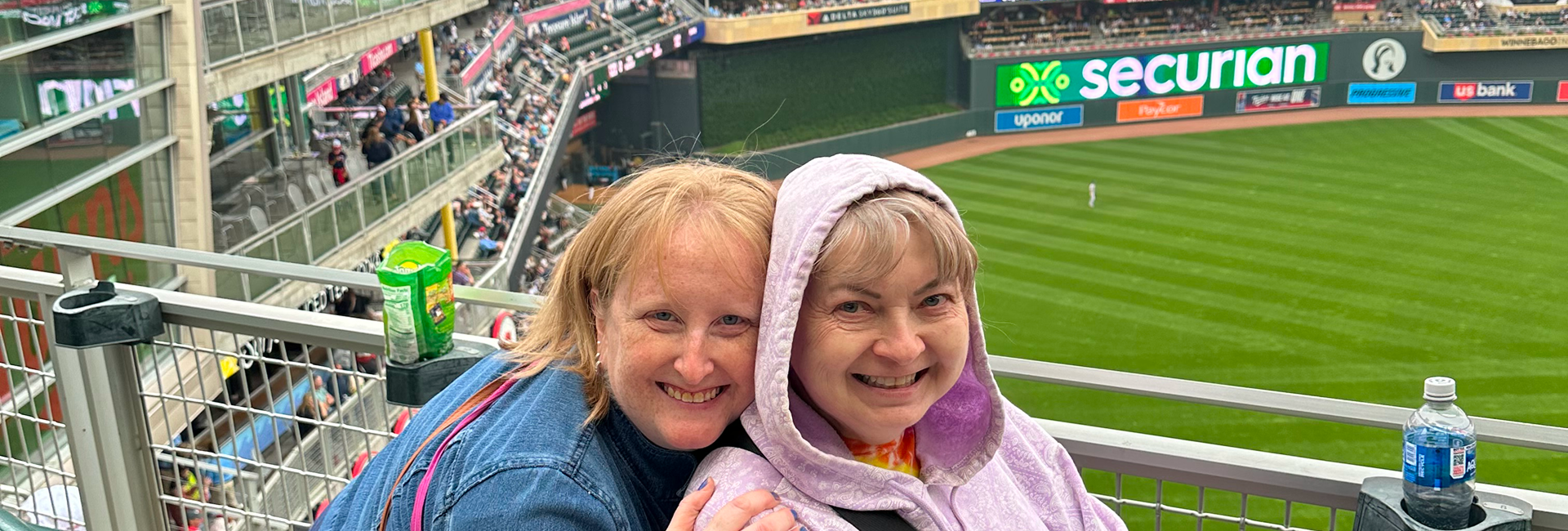 Two smiling people bundled up at a baseball stadium.